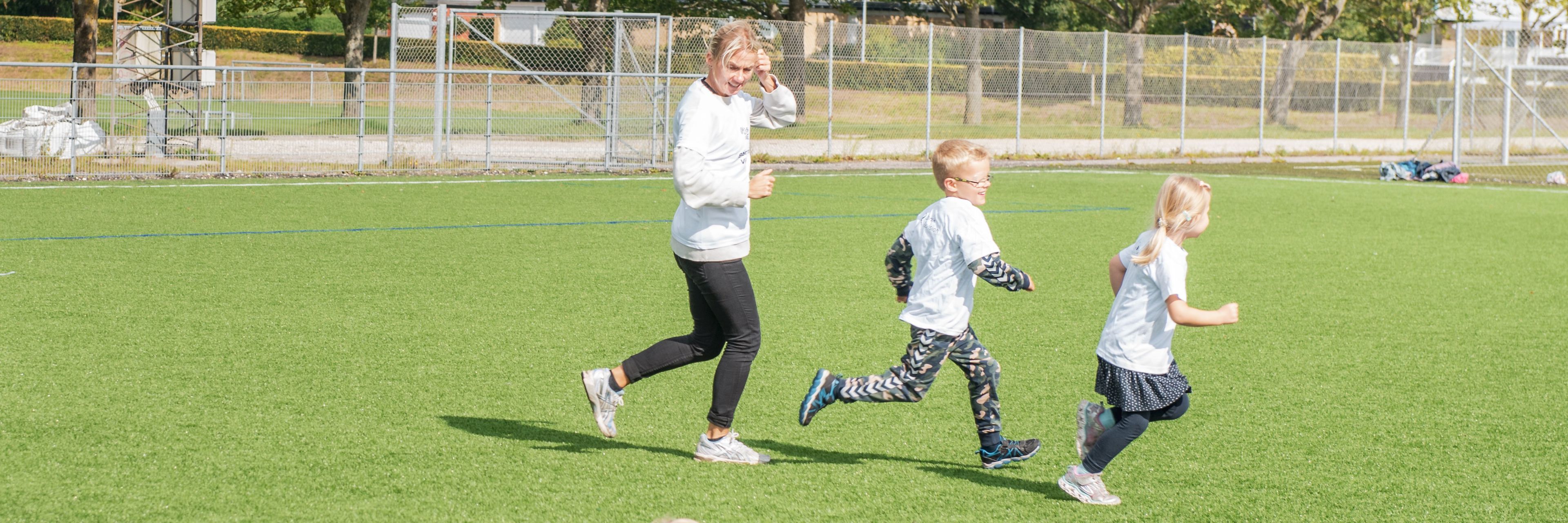 Børn og træner løber på fodboldbane