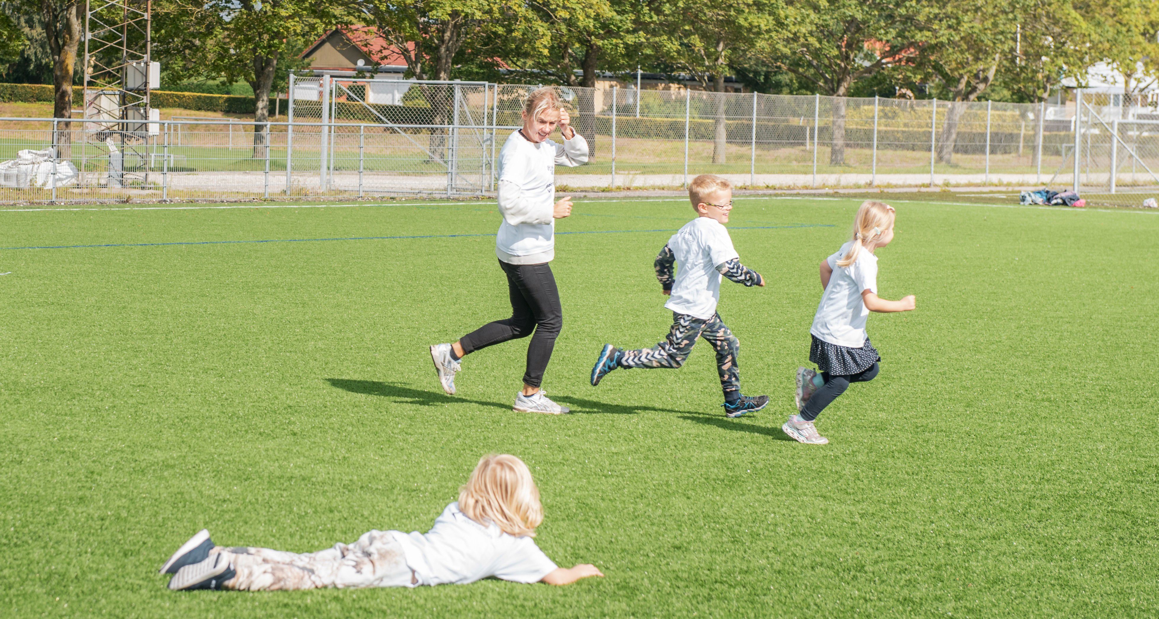 Børn og træner løber på fodboldbane