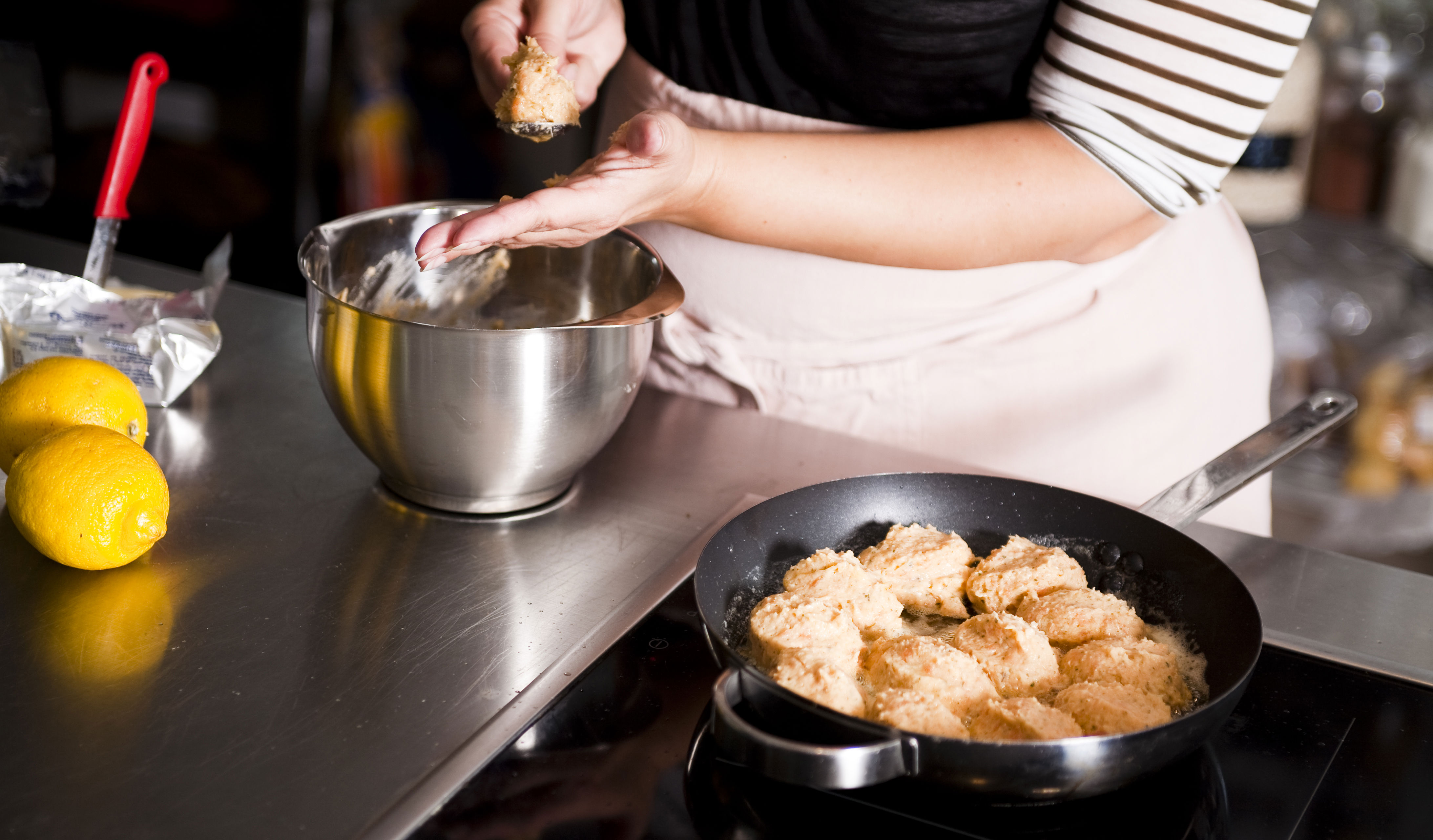 Kvinde former kødboller og steger dem på pande.