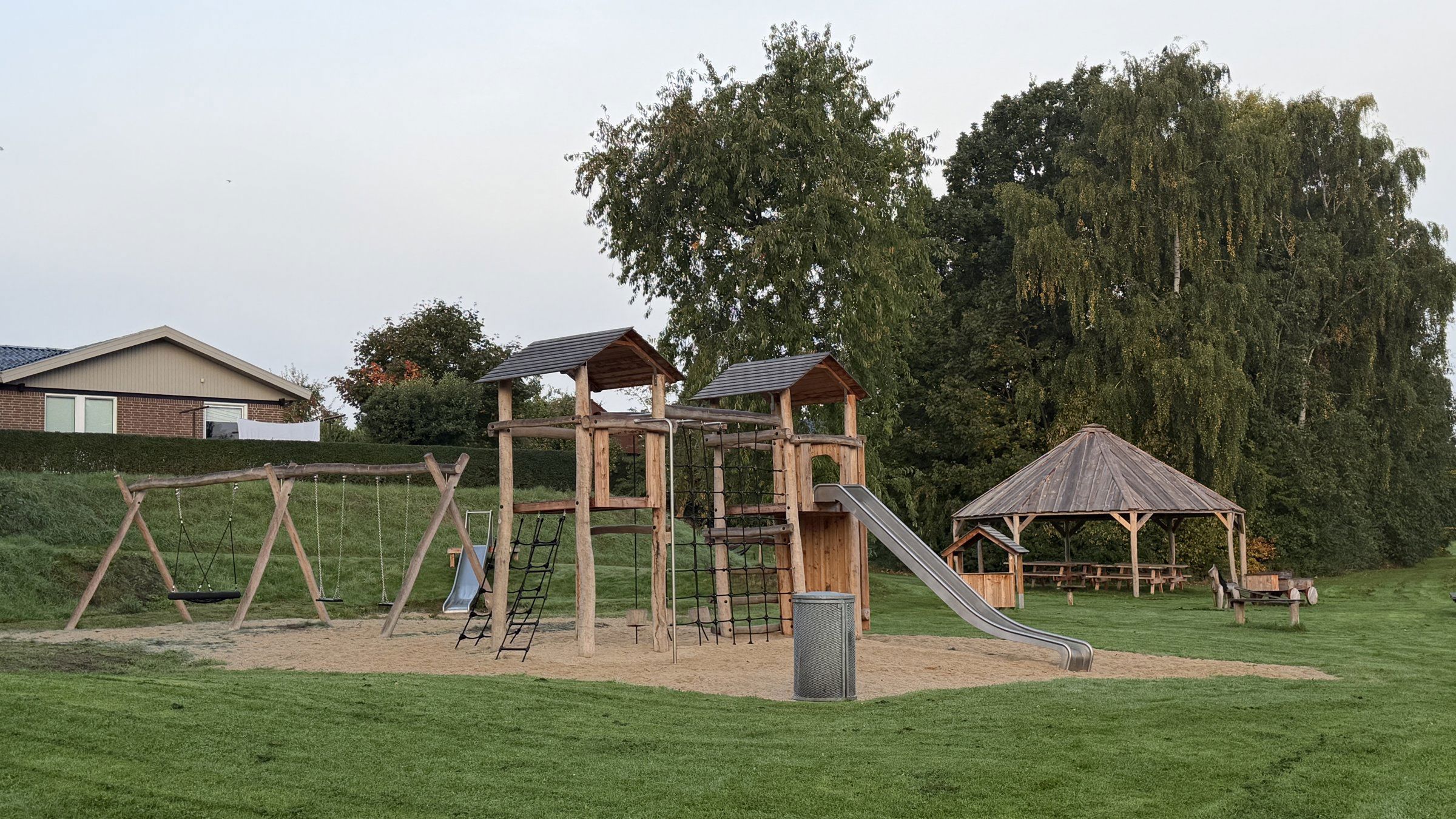 Legepladsen i Helstedparken med gynger, et legetårn med rutsjebane og en pavillon